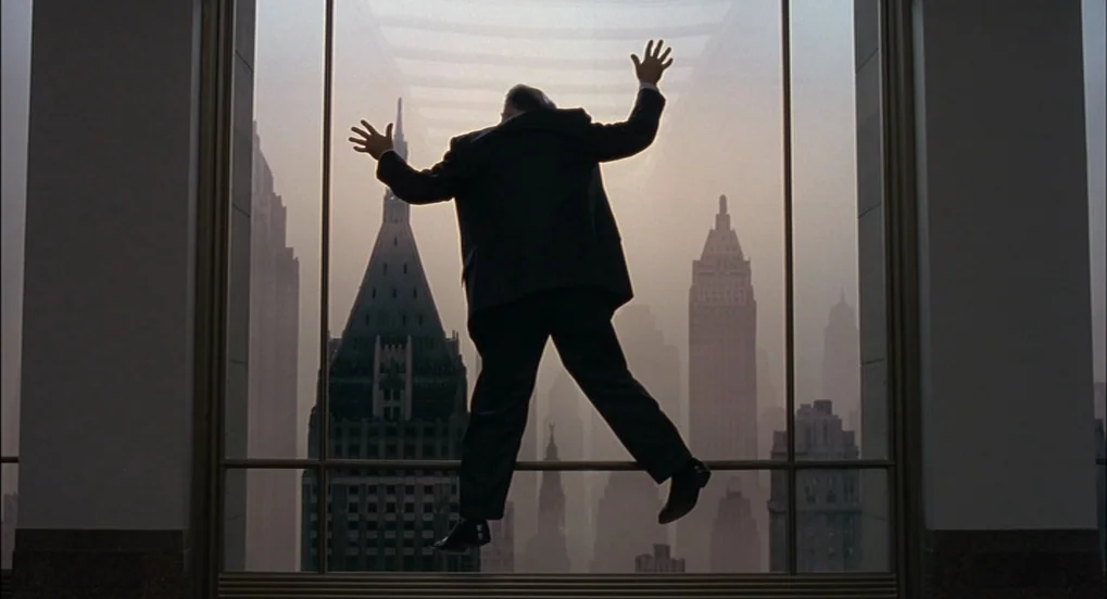 The Hudsucker Proxy (1994) movie still: fullbody — A high-rise office interior features a large pane of glass overlooking a city skyline. A man in a…