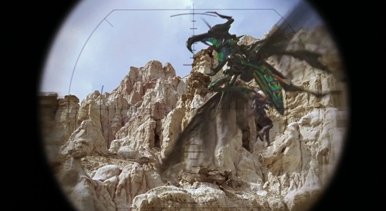 Starship Troopers (1997) movie still: wide — A rugged desert canyon features light-colored, weathered rock formations under a clear sky. A winged,…
