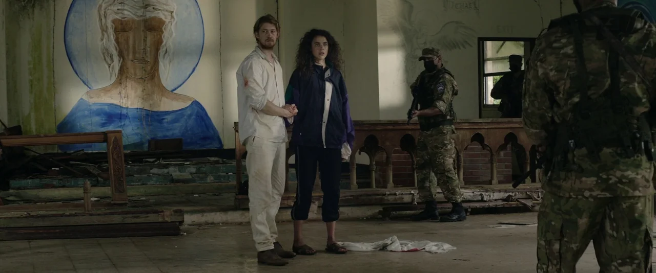 Stars At Noon (2022) movie still: fullbody — An abandoned interior space features a faded mural of an angel on the wall. A young man and woman stand…