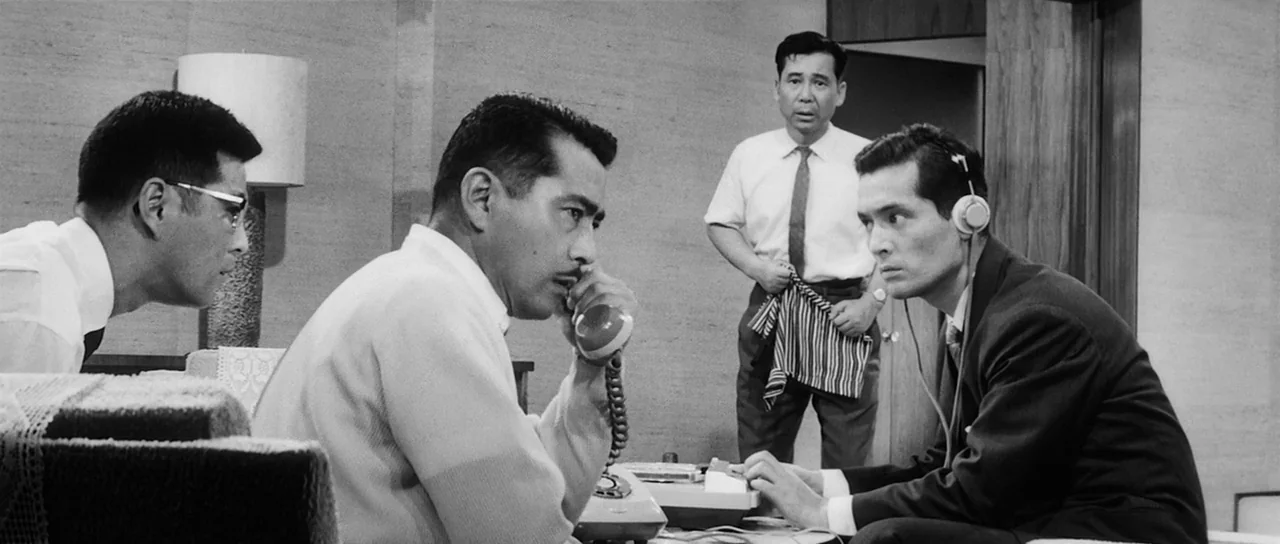 High and Low (1963) movie still: medium — An office interior features four men organized around communication equipment and a rotary phone. They are…
