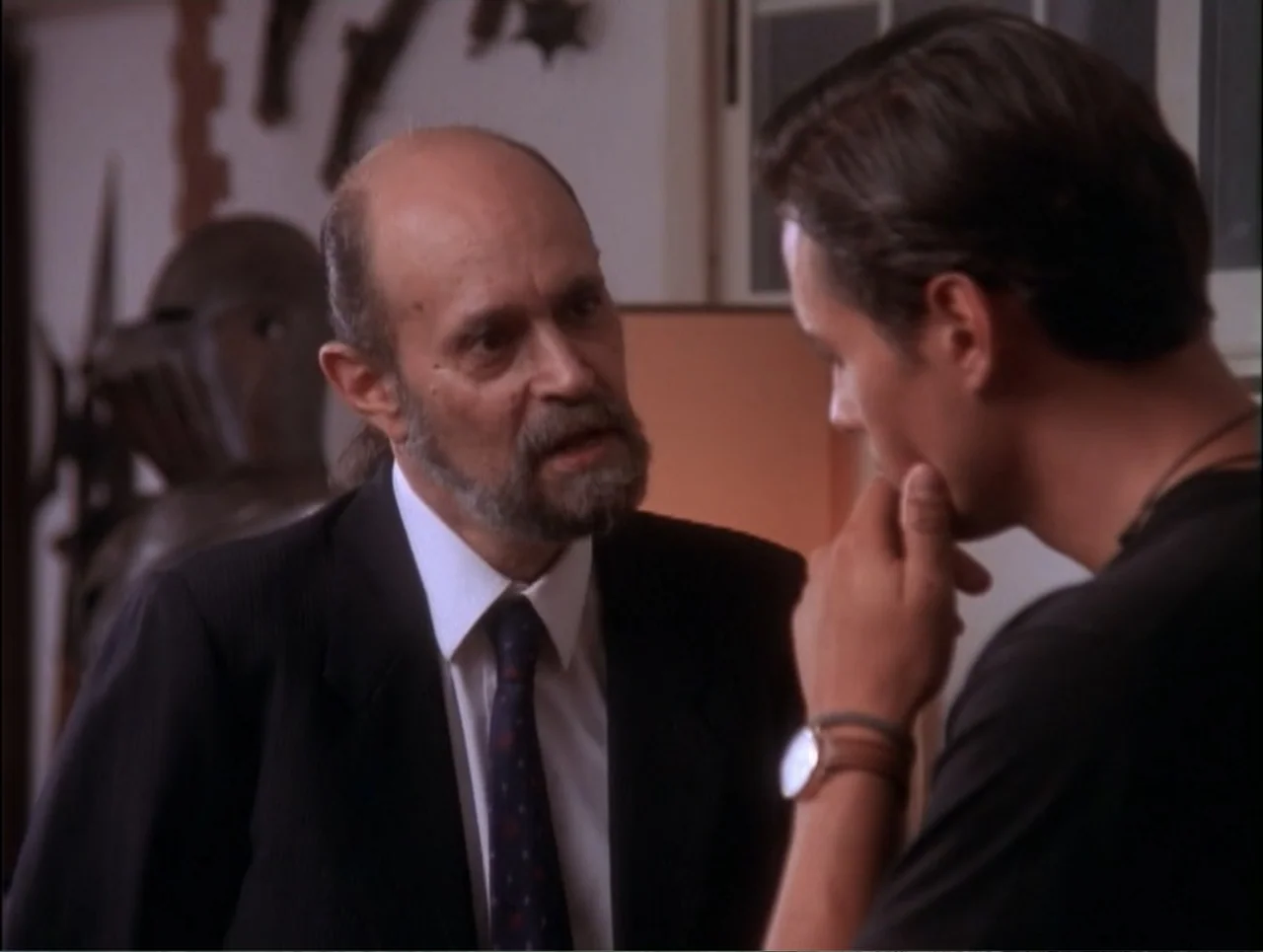 Code Name: Wolverine (1996) movie still: medium — An interior office space features a wall display of decorative medieval armor helmets. An older…
