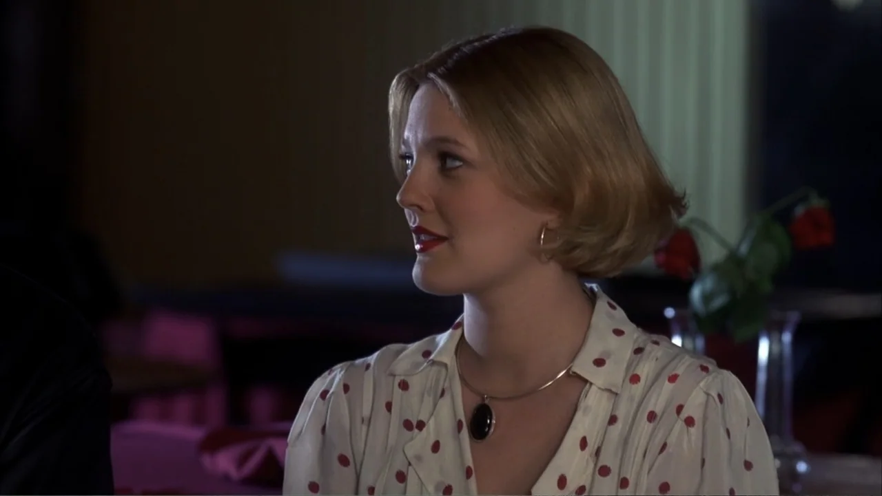 The Wedding Singer (1998) movie still: medium — A dark restaurant interior with a table set for dining. A young woman with blonde hair sits at the…
