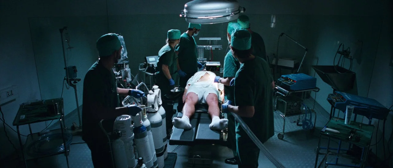 Sound of Noise (2010) movie still: wide — A clinical operating theater contains medical equipment and a patient centered on a table. Several…