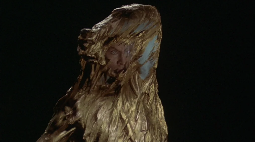 Danger Diabolik (1968) movie still: closeup — A dark, empty space frames a figure completely covered in thick, textured gold substance. A human face…