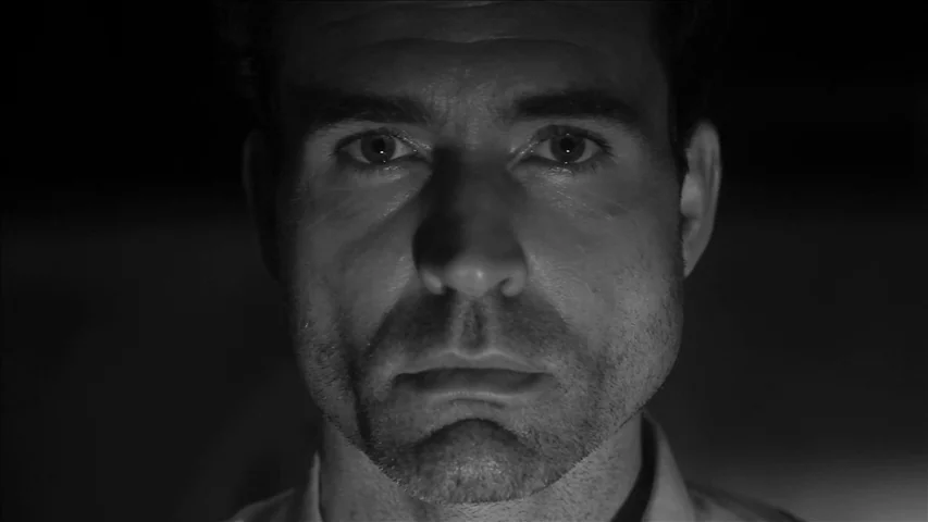 Keyhole (2011) movie still: closeup — A man's face is positioned in a dark environment with no background details visible. The subject stares ahead…