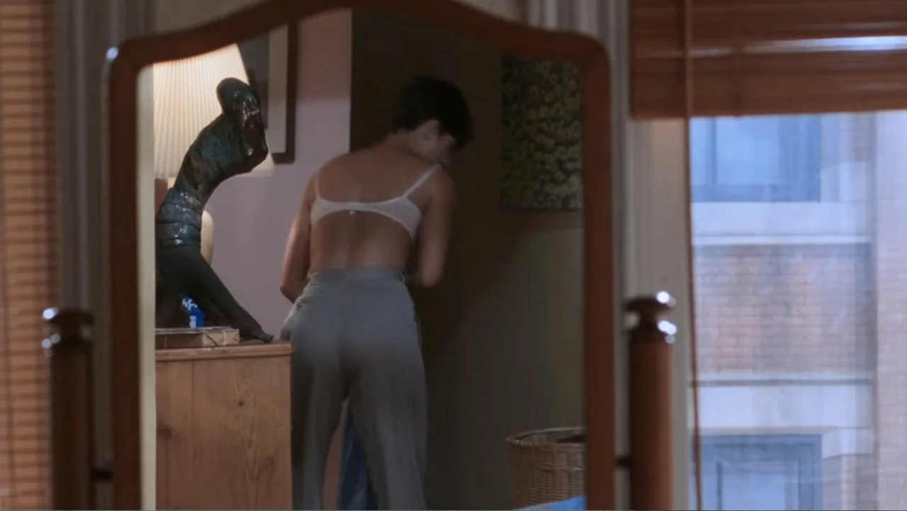 Ghost (1990) movie still: medium — A bedroom interior features a wood-framed mirror reflecting a woman in partial attire. The woman stands near a…