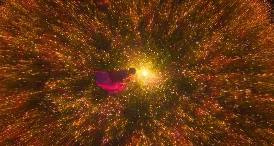 Encanto (2021) movie still: wide — A person floats within an abstract field of radiating golden light and particles. The subject drifts horizontally…
