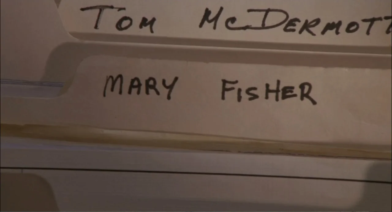 She-Devil (1989) movie still: closeup — A close-up view shows two stacked Manila file folders inside an office cabinet. The name Mary Fisher is…