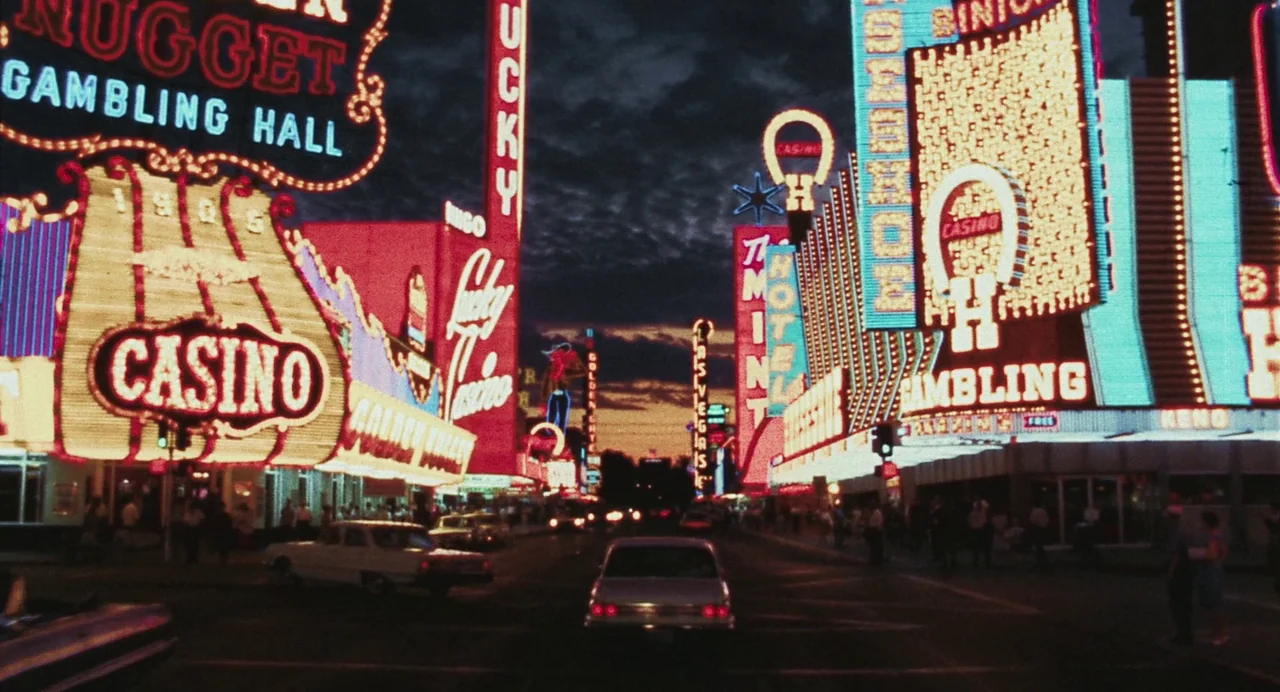 Priscilla (2023) movie still: wide — A vibrant downtown district at twilight features dense clusters of iconic neon casino signage. Vintage…