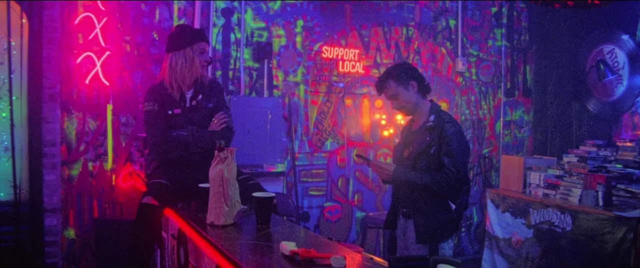 Christmas Bloody Christmas (2022) movie still: medium — A dimly lit bar interior features walls covered in fluorescent neon graffiti and artwork. A…