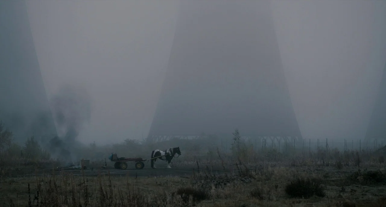 The Selfish Giant (2013) movie still: wide — An open field contains patches of dry vegetation and rising plumes of dark smoke. A horse stands…