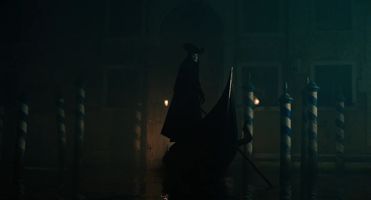 A Haunting In Venice (2023) movie still: wide — A foggy Venetian canal at night features striped mooring poles flanking a dark passage. A lone…