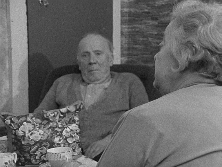 Cathy Come Home (1969) movie still: medium — A quiet indoor space features an elderly man seated while a woman faces him. A floral pattern handbag…