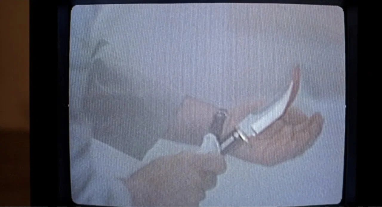 F/X2 (1991) movie still: closeup — A close-up shot captured from a low-resolution television screen shows a pair of hands. A person holds a large…