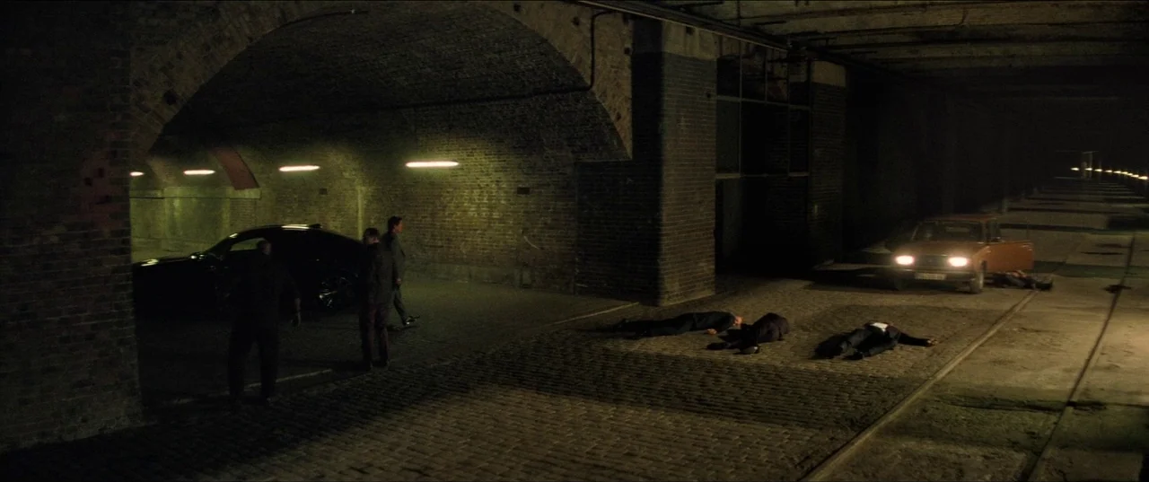 Mission: Impossible – Fallout (2018) movie still: wide — A dark, brick-lined underpass with arched ceilings and a cobbled ground surface. Three men…