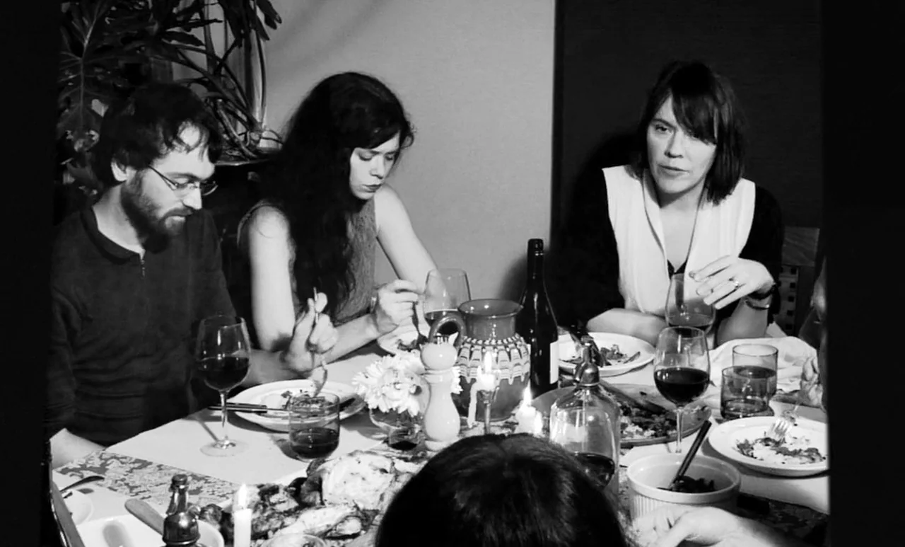Go Down Death movie still: medium — A group of people sits around a dinner table covered with plates and glasses. The diners are mid-meal in a dimly…
