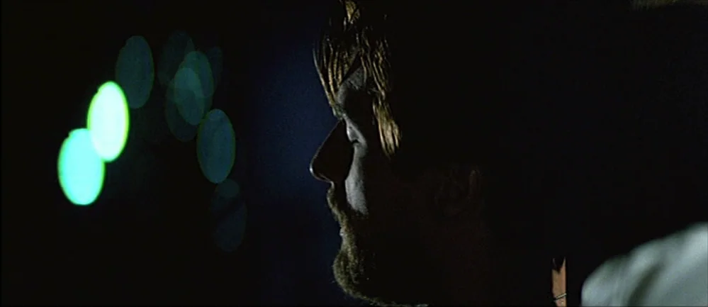 The Deer Hunter (1978) movie still: closeup — A dark, interior setting with soft green out-of-focus light sources on the left side. A man with a…