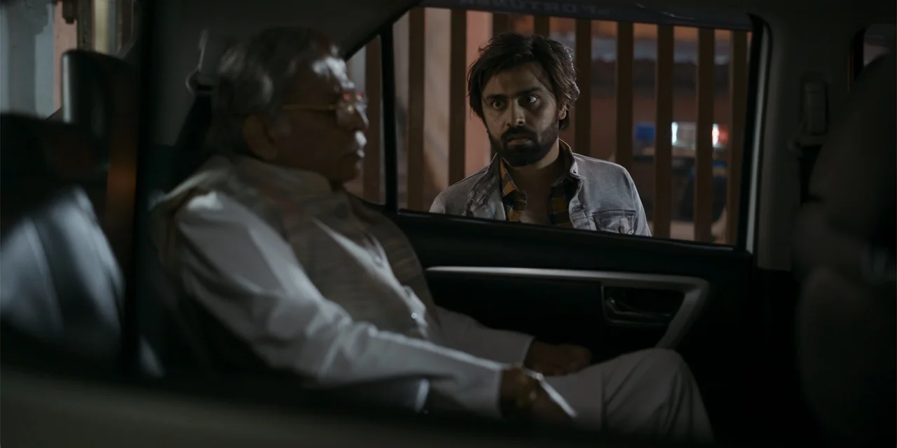 Dry Day (2023) movie still: medium — A dark car interior at night viewed from the back seat through the window. An older man sits inside while a…