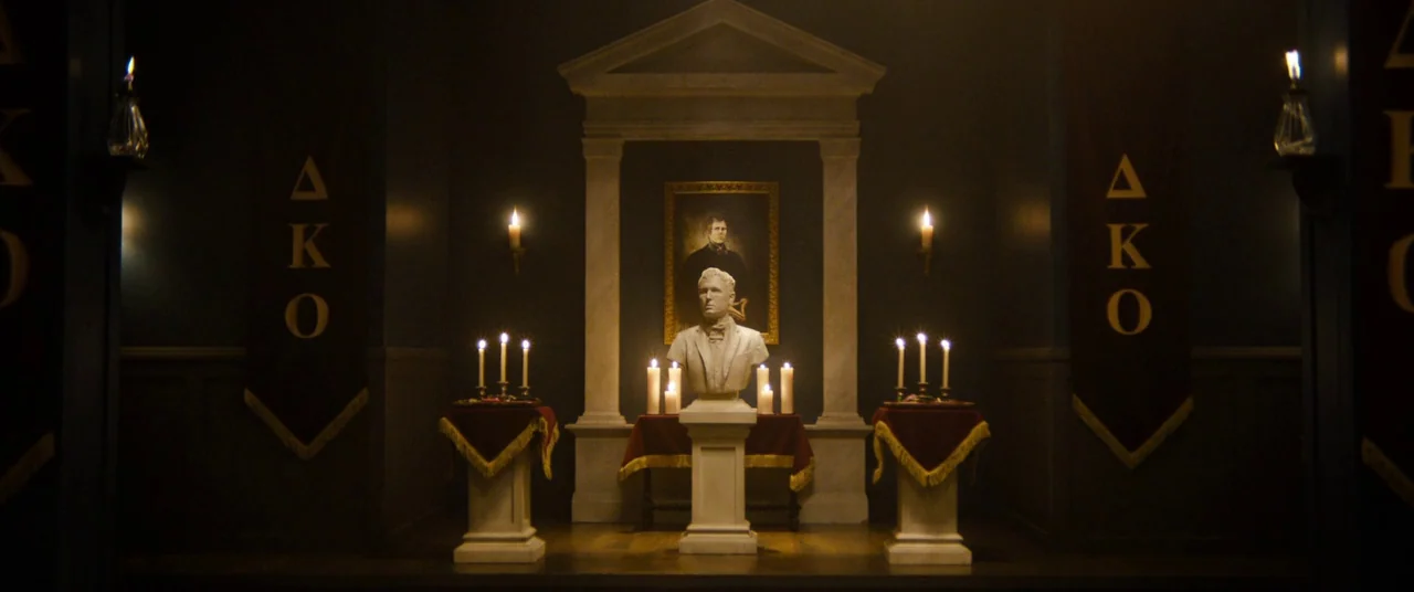 Black Christmas (2006) movie still: wide — A dark, symmetrical ritual room features a central stone bust on a pedestal. Two tall banners flank the…