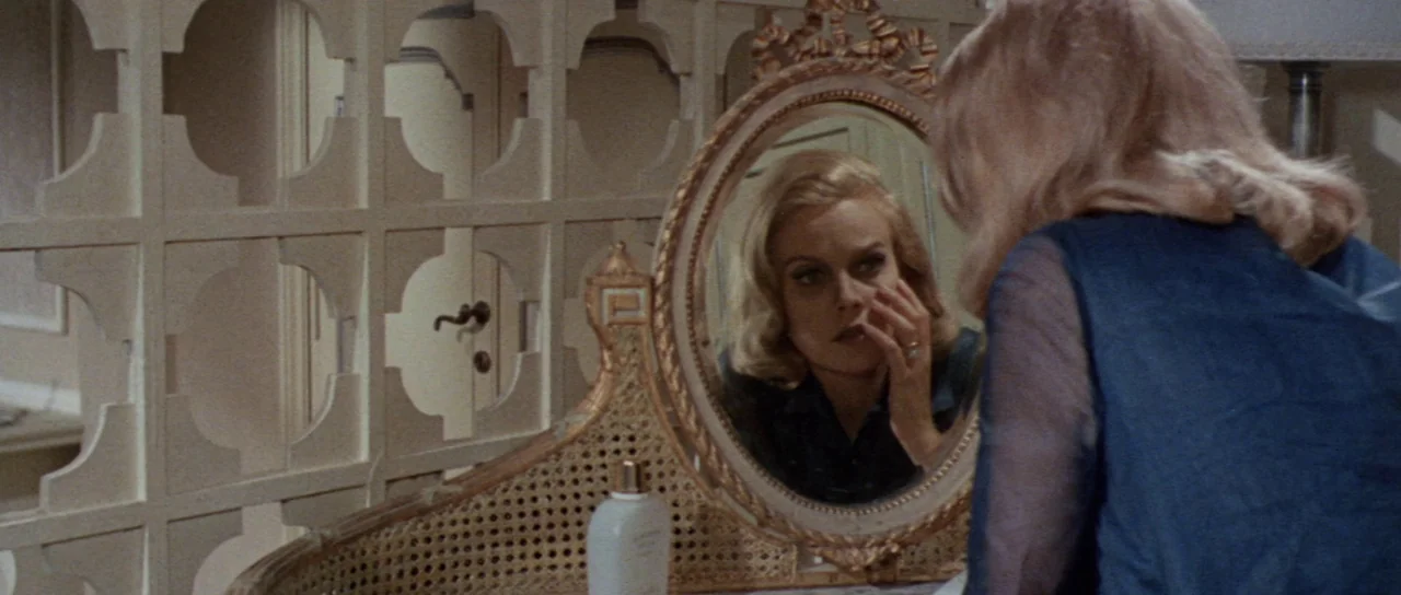 Orgasmo (1969) movie still: medium — A vanity table holds a wicker-framed oval mirror with decorative wooden elements. A blonde woman faces the…
