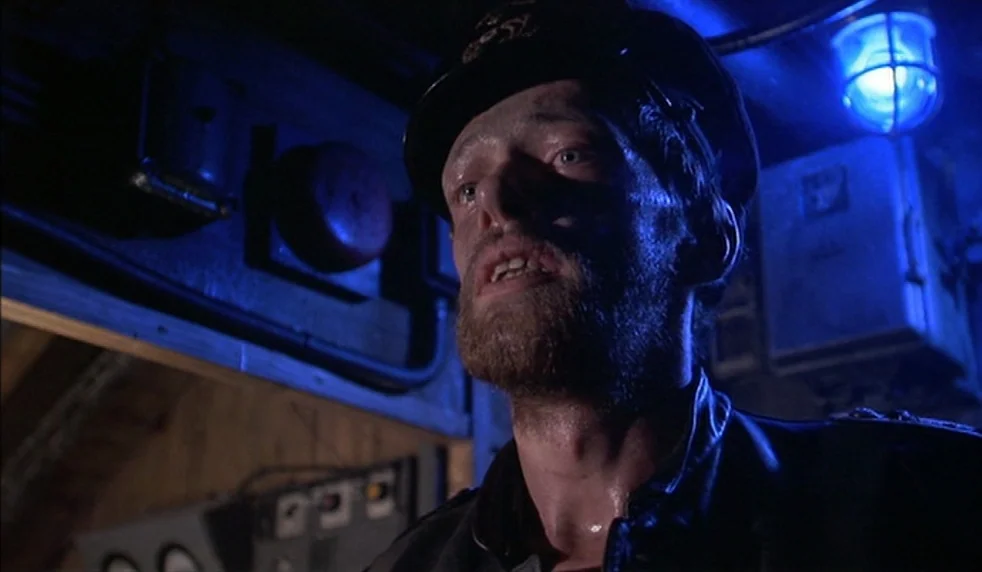 Das Boot (1981) movie still: closeup — A cramped, metallic submarine interior features exposed pipes and mechanical equipment in the background. A…