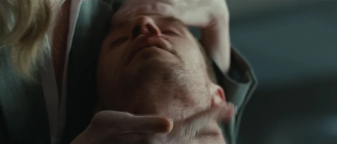 Slackers (2002) movie still: closeup — A close-up view shows a person holding the jaw and forehead of a man. The man's eyes are closed while hands…