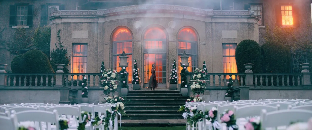 Ready or Not (2019) movie still: wide — A stone terrace features rows of white chairs facing a large, lit mansion facade. A lone figure stands…