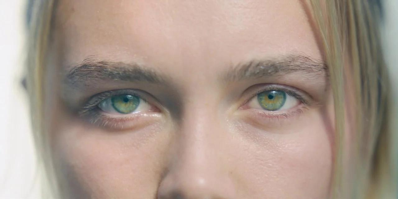 Midsommar (2019) movie still: closeup — A close-up shot focusing on the face of a person in a bright room. The subject stares straight ahead with…