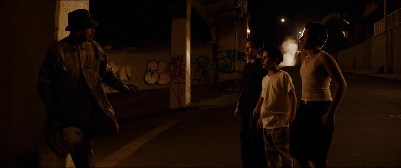 El Chicano (2018) movie still: wide — An urban concrete underpass at night is illuminated by a distant streetlamp. A man stands on one side…