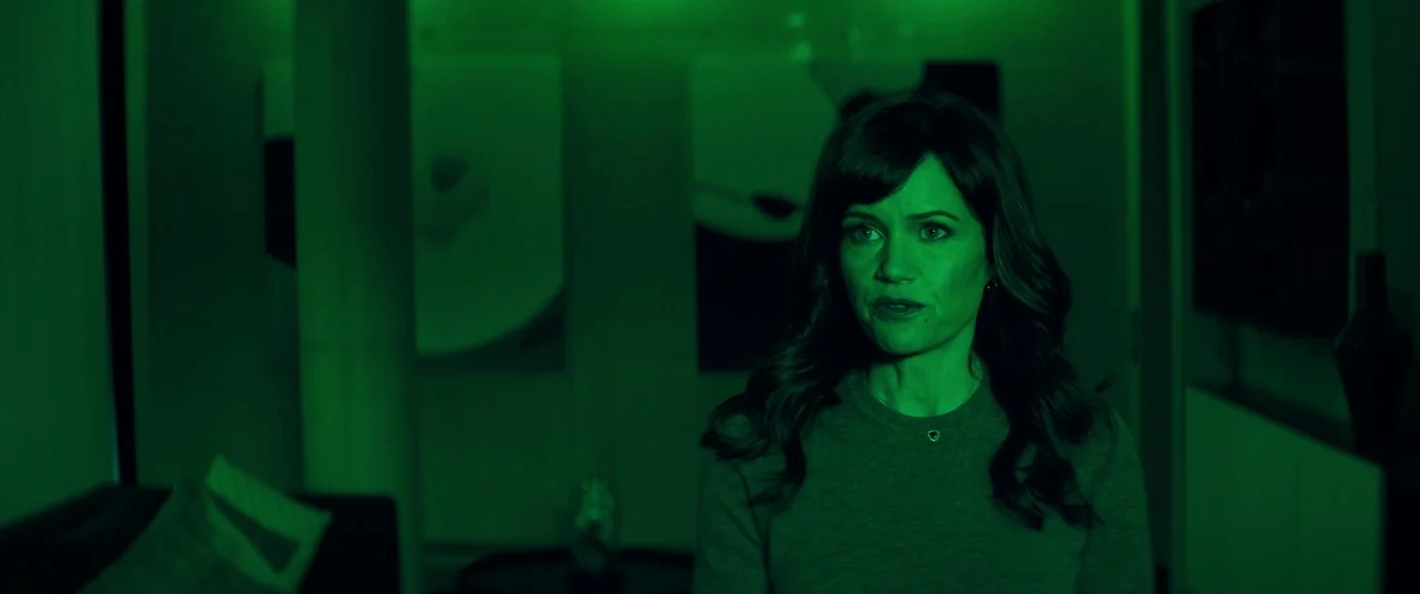 Elizabeth Harvest movie still: medium — A modern dark room contains a woman standing in the center of the frame. The woman is illuminated only by a…