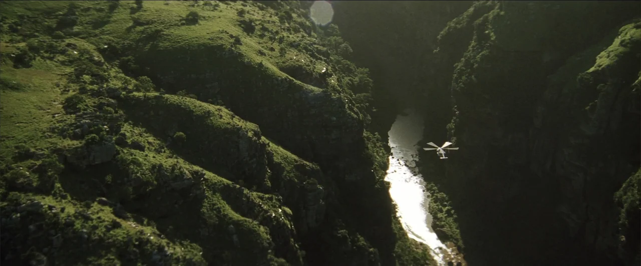 Blood Diamond (2006) movie still: establishing — A deep rocky river canyon covered in green grass and steep cliffs. A helicopter flies over the…