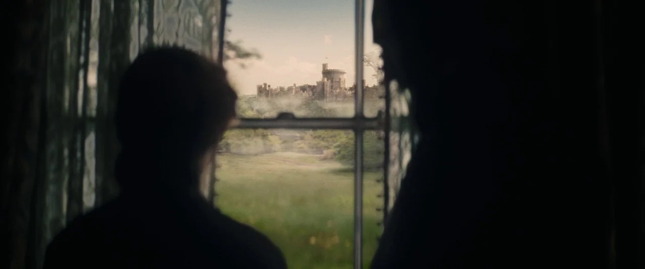 The Invisible Woman (2013) movie still: medium — A dimly lit room faces out onto a lush green landscape with a castle. Two silhouettes stand in the…