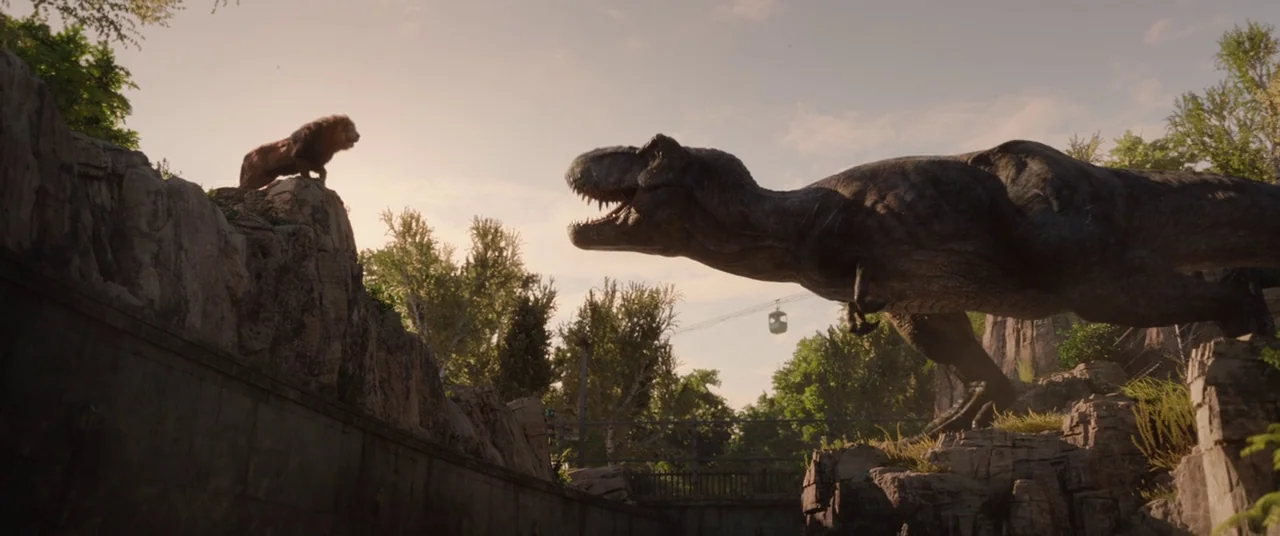 Jurassic World: Fallen Kingdom (2018) movie still: wide — A rocky enclosure featuring a T-rex standing near a lion perched on a ledge. A small cable…