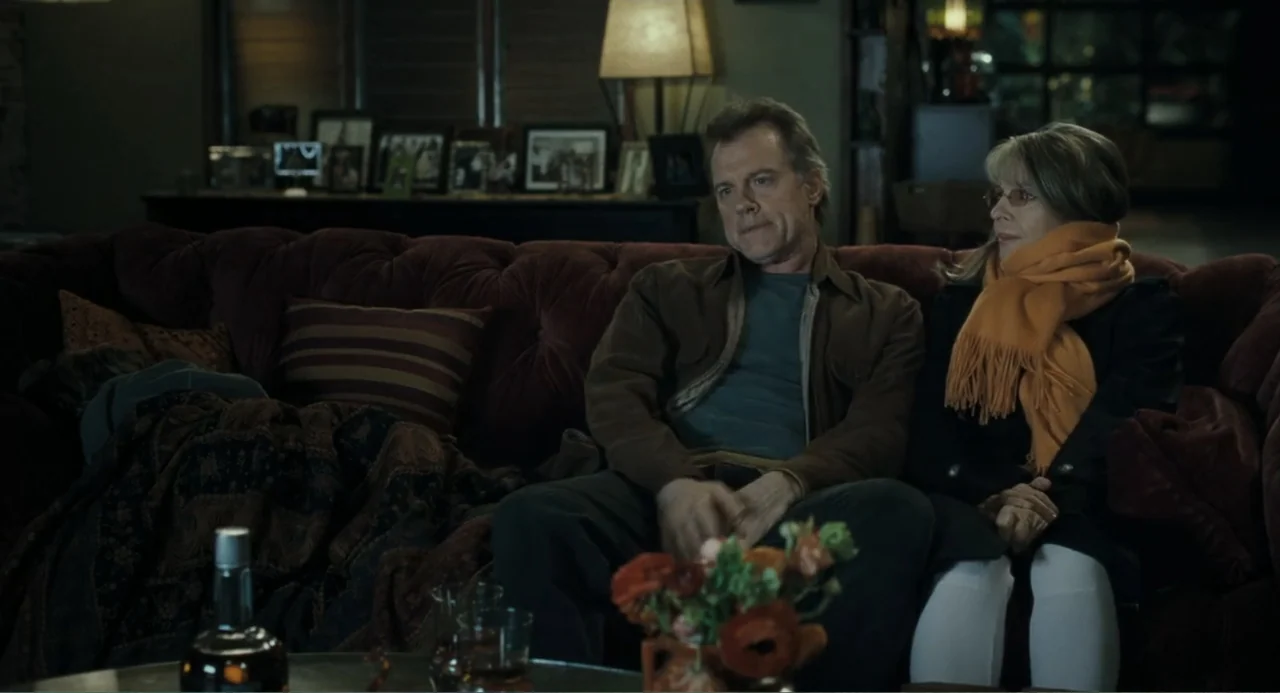 Because I Said So (2007) movie still: medium — A dimly lit room contains a plush dark red tufted sofa and a coffee table. A middle-aged couple sits…