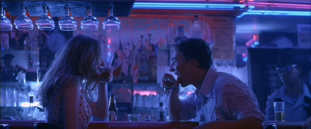 Down In The Valley (2005) movie still: medium — A dimly lit bar glows with intense blue and pink neon light reflections. A man and woman sit facing…