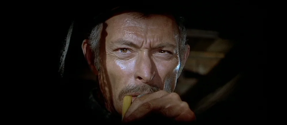 For A Few Dollars More (1965) movie still: closeup — A dark, unidentifiable space hides all background detail behind a man's face. The man maintains…