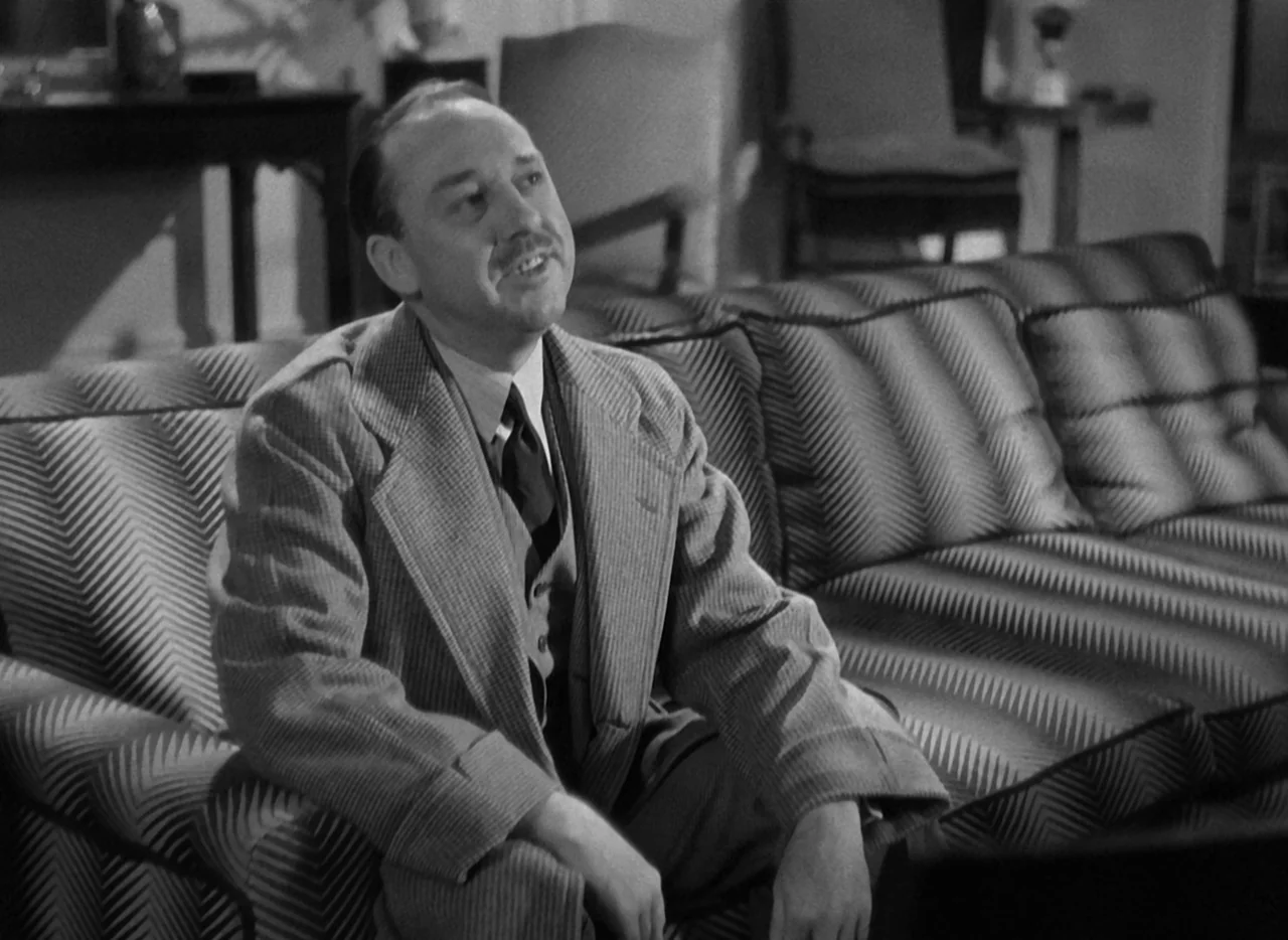 The Thin Man (1934) movie still: medium — A well-furnished room featuring a patterned chevron-style sofa and dim ambient lighting. A middle-aged man…
