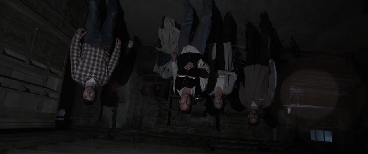 The Conjuring (2013) movie still: fullbody — A dark, unfinished basement with stone walls and wooden structural supports. Four individuals stand…