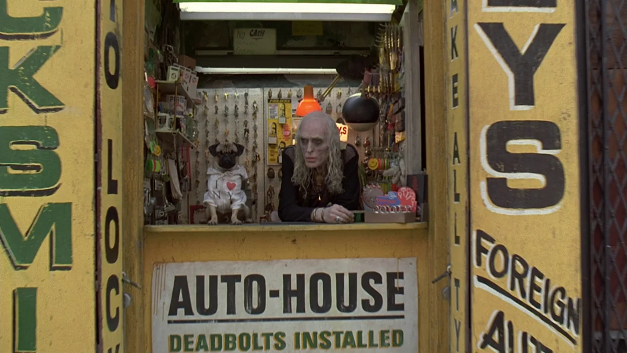 Men In Black (1997) movie still: medium — A small, cluttered urban service stall with yellow-painted walls covered in hand-painted signage. A thin…