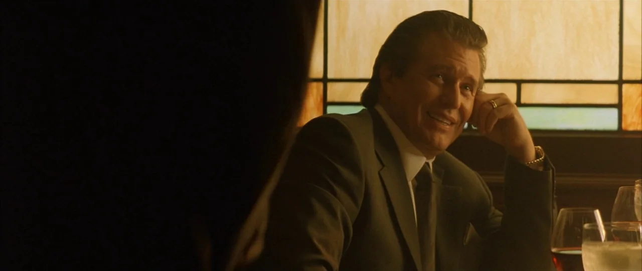 Training Day (2001) movie still: medium — A man sits in a booth in front of an illuminated stained glass window. He is smiling while looking at an…