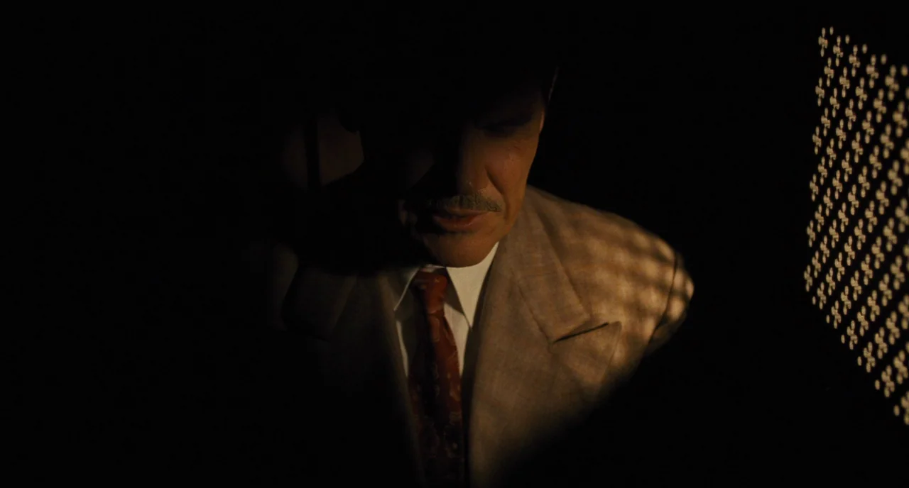 Hail, Caesar! (2016) movie still: medium — A dimly lit telephone booth is characterized by dark shadows and a patterned light source. A man in a tan…