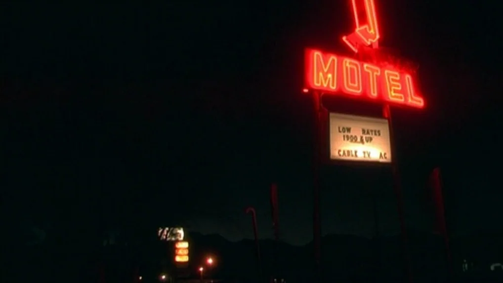 Land of Plenty (2004) movie still: establishing — A tall metal neon motel sign illuminates the dark surroundings of a roadside property. The sign…