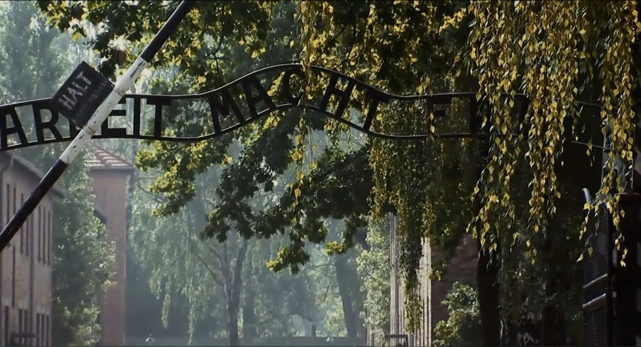 Pope Francis: A Man of His Word (2018) movie still: establishing — A wrought iron gate bearing the inscription Arbeit Macht Frei stands in a…