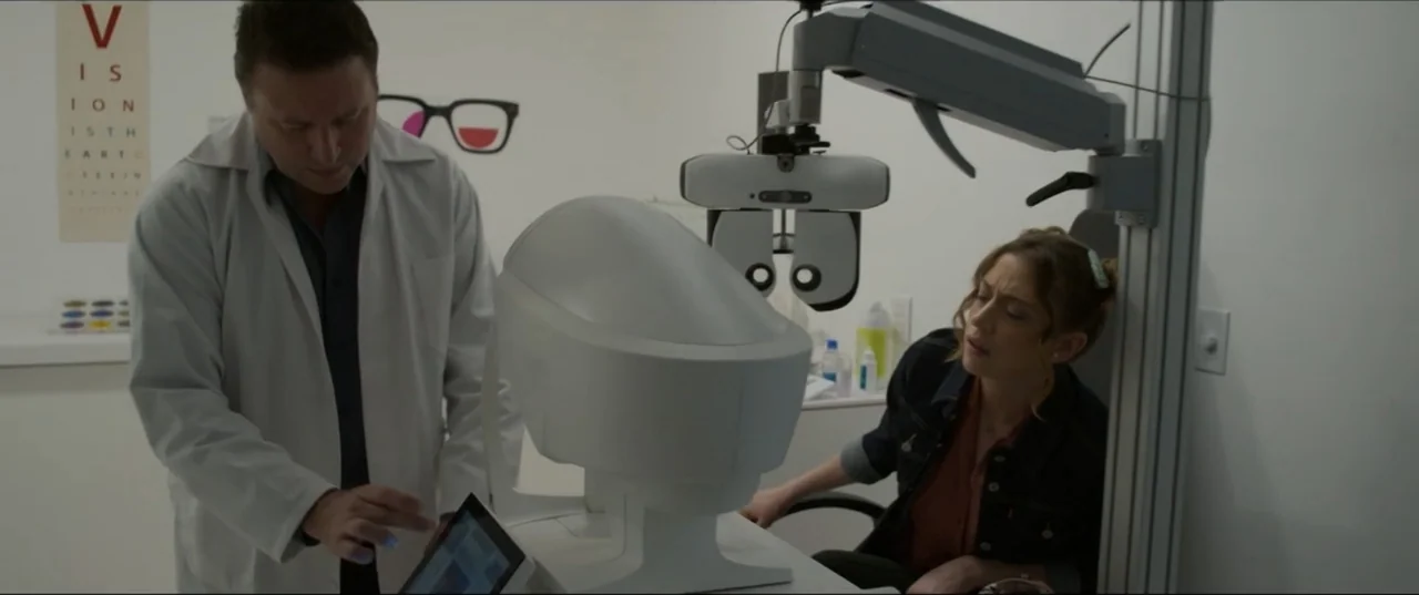 Can't Quit Mom (2022) movie still: medium — An optometrist office features a large white medical device and a wall vision chart. A male doctor…