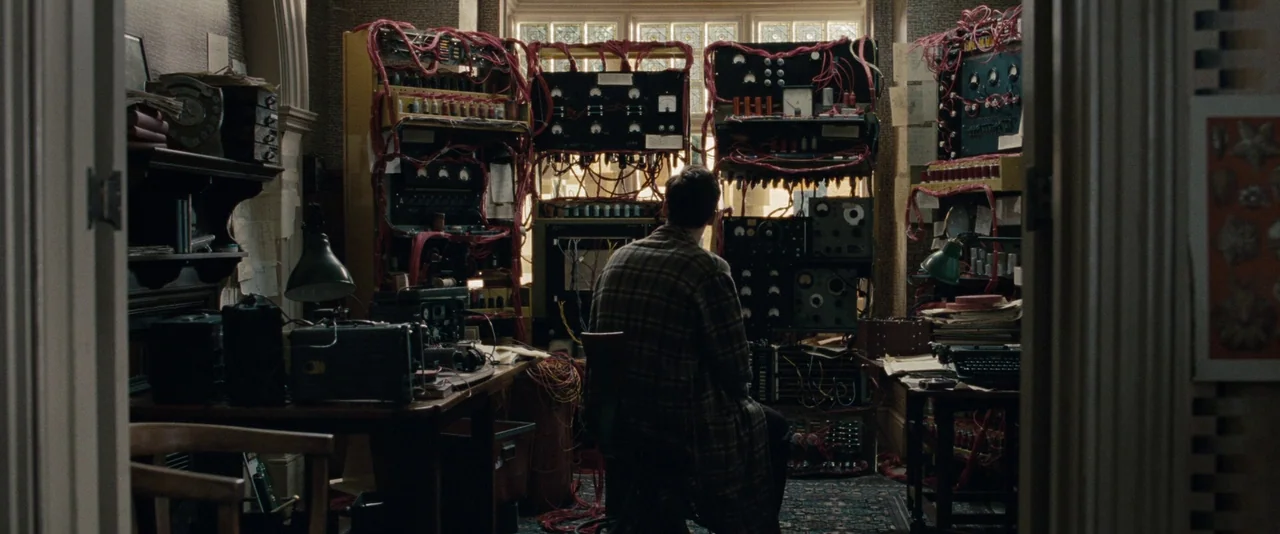 The Imitation Game (2014) movie still: medium — A cluttered room filled with antique electrical equipment and tangled red wiring. A man sits at a…