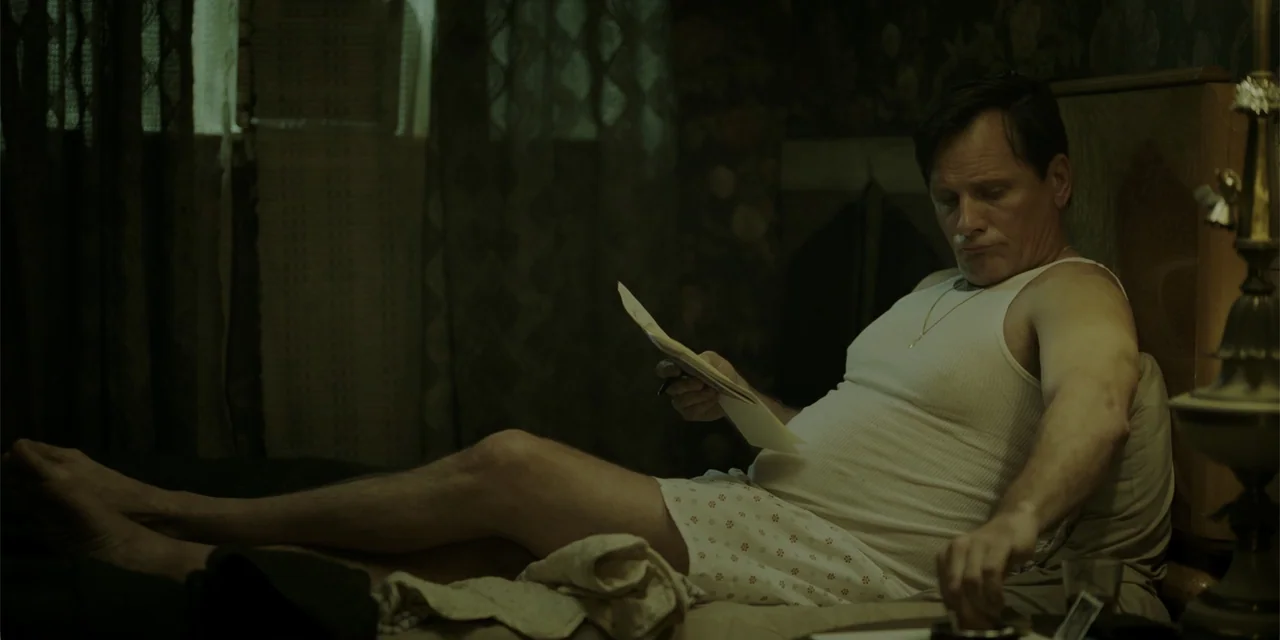 Green Book (2018) movie still: medium — A dimly lit bedroom features floral patterned wallpaper and a bedside lamp with a shade. A man sits upright…