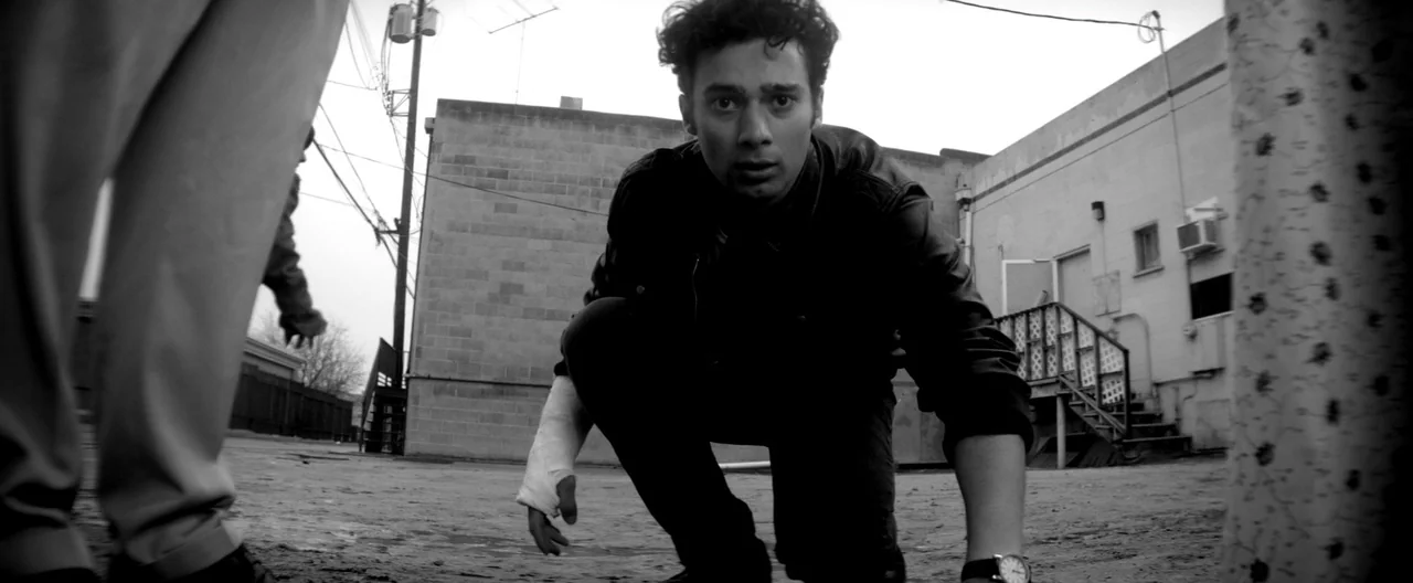 A Girl Walks Home Alone at Night (2014) movie still: fullbody — A paved area behind a building features a cinder block wall and stairs. A young man…