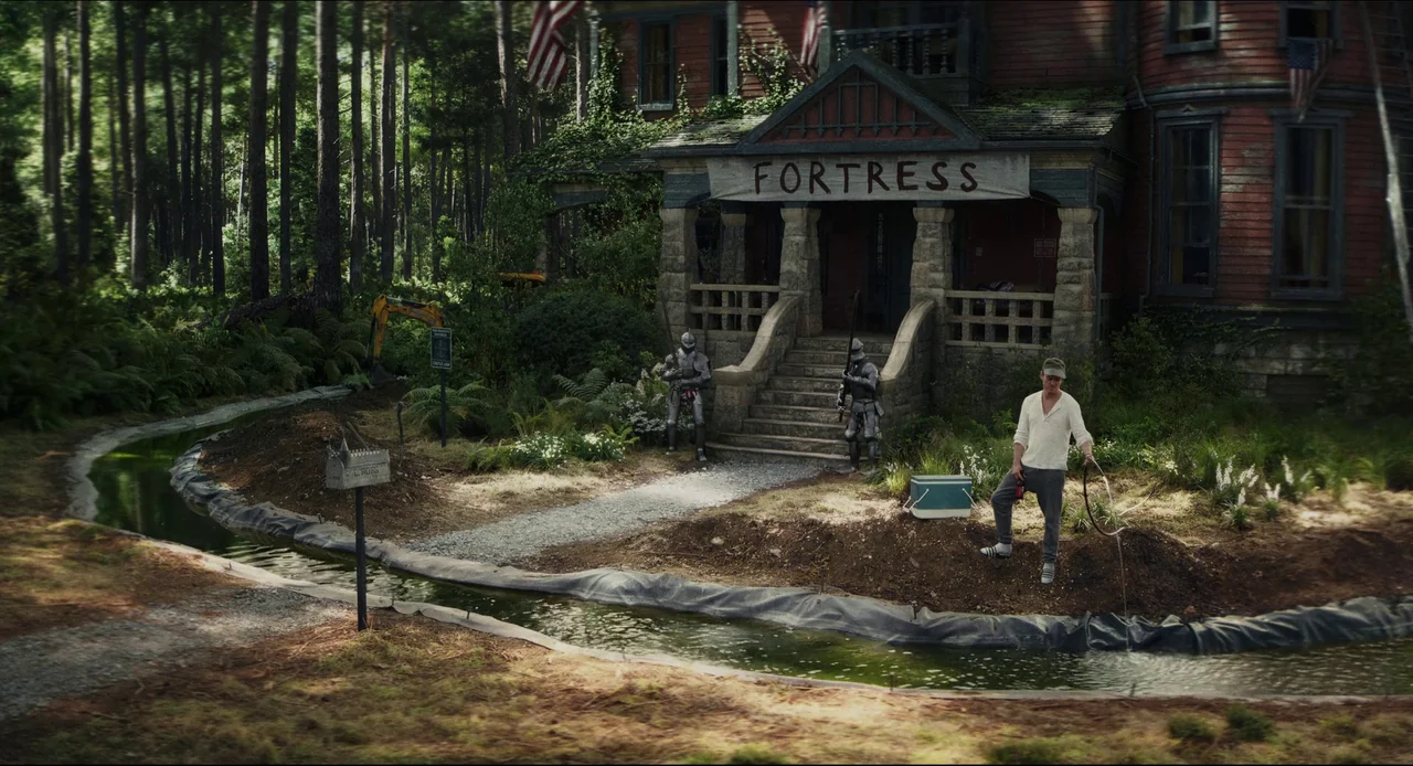Wake Up Dead Man (2025) movie still: wide — A weathered wooden house with a sign reading Fortress stands behind a dirt-excavated yard. A man in…
