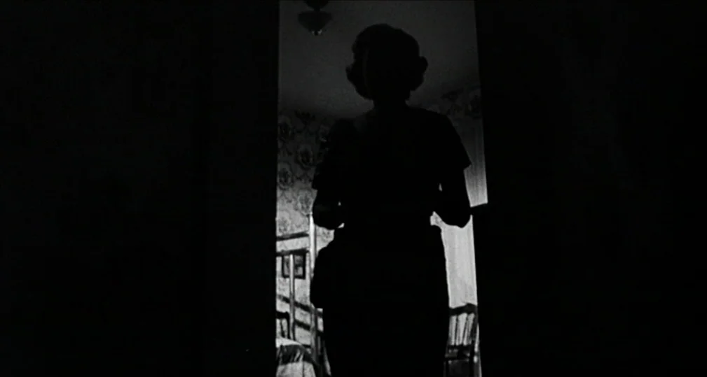 Midnight Cowboy (1969) movie still: medium — A dark figure stands in a doorway looking into a illuminated room. The room beyond features floral…
