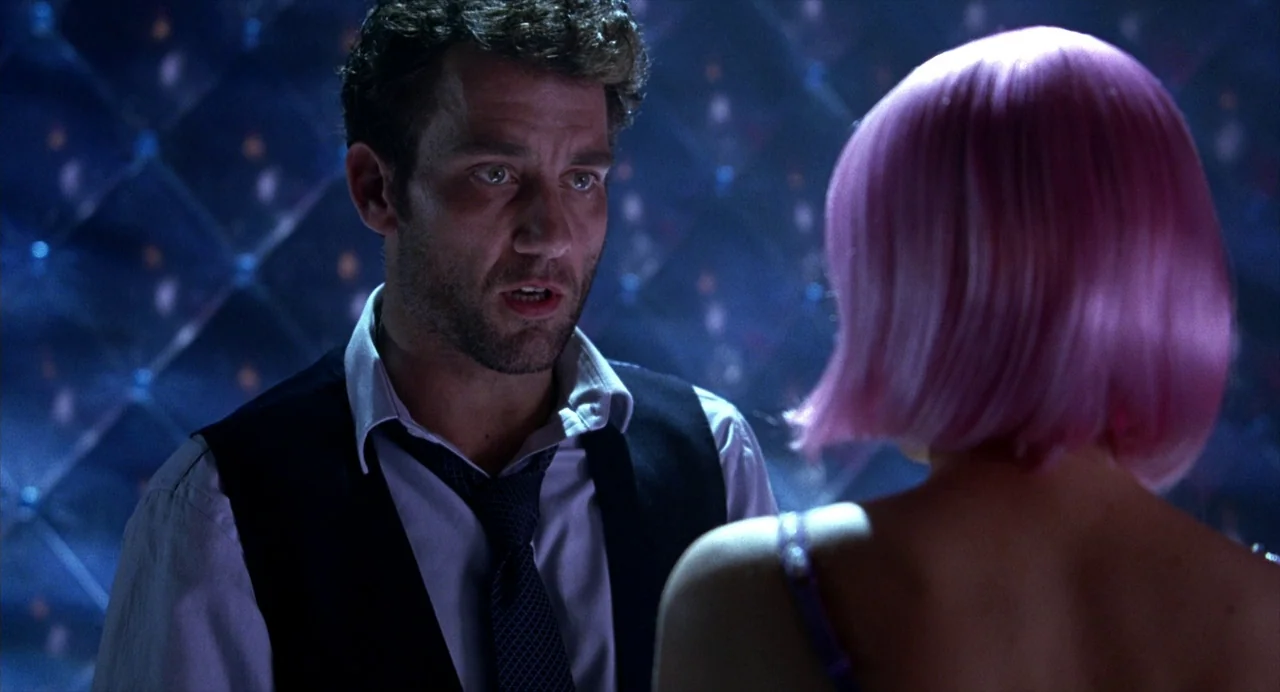 Closer (2004) movie still: medium — A dark, dimly lit club environment features a quilted wall with reflective accents. A man in formal wear stands…